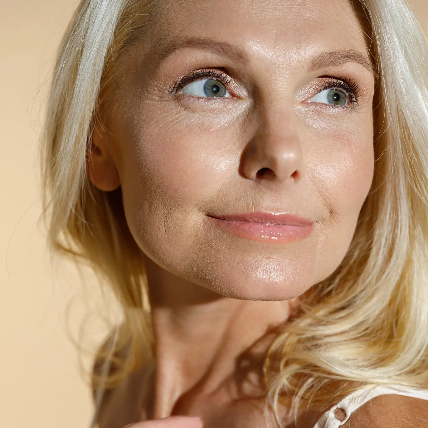 Close-up of a woman with blonde hair and blue eyes against a beige background