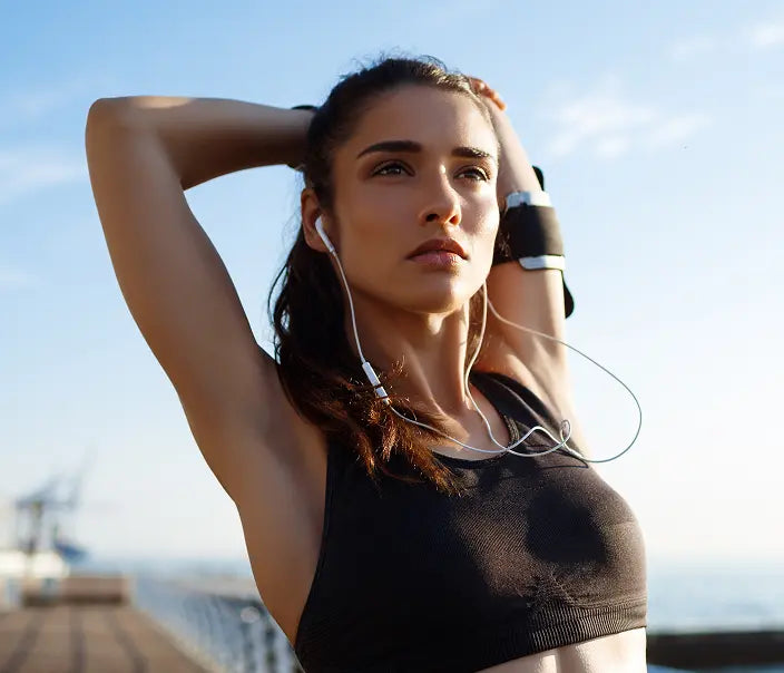 Woman exercising outdoors with earphones, wearing a black sports bra.
