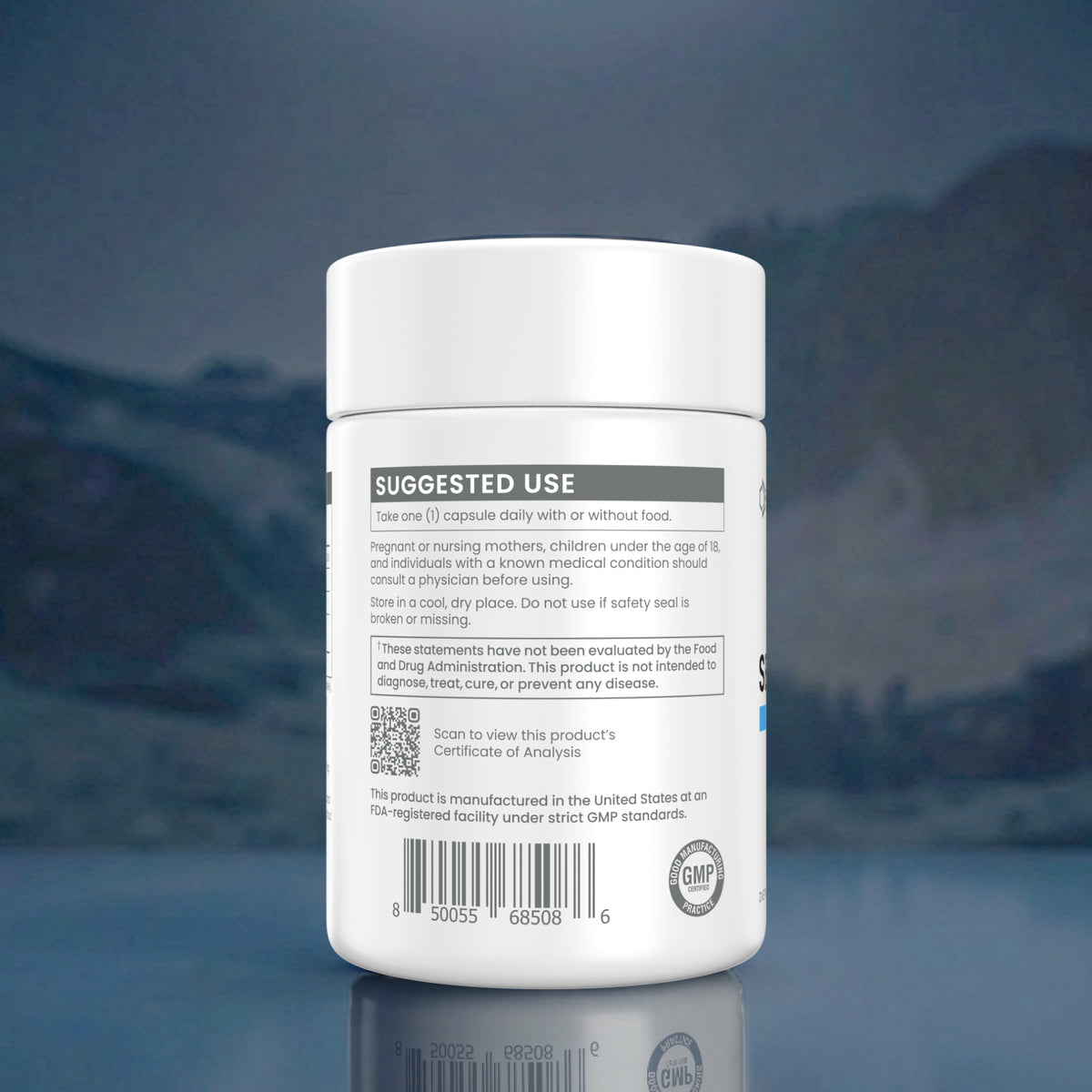 A white plastic supplement bottle shown from the back, featuring a detailed 'SUGGESTED USE' label with text, a QR code, and a barcode. The bottle is centered against a dark, moody background with a soft blue glow and a subtle reflection on the surface below.