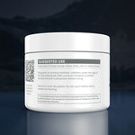 A white plastic jar of dietary supplement powder with a white lid, featuring a detailed 'SUGGESTED USE' label with text, a QR code, and warning boxes, set against a dark blue gradient background with a soft reflection below.