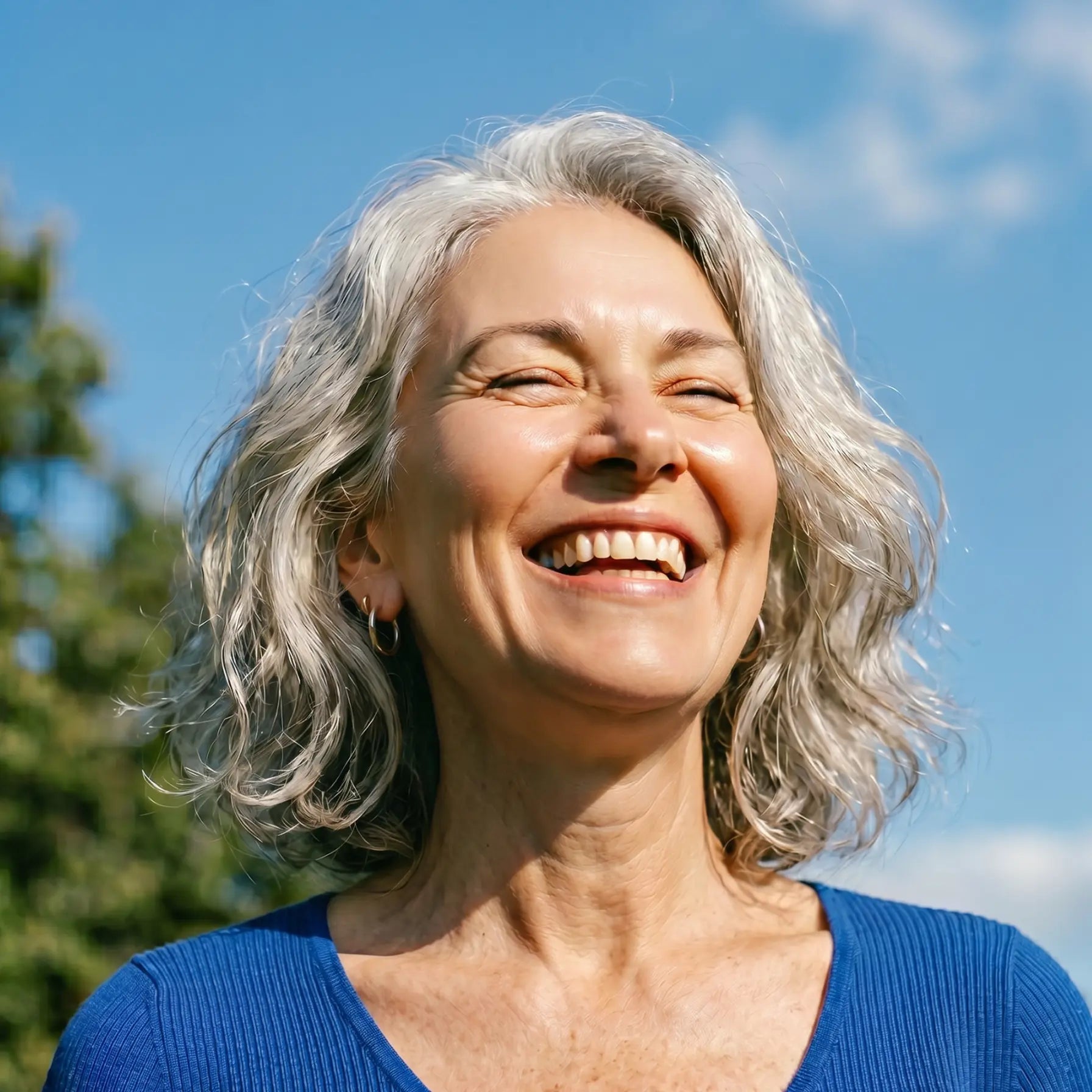 Woman with gray hair smiling outdoors against a blue sky