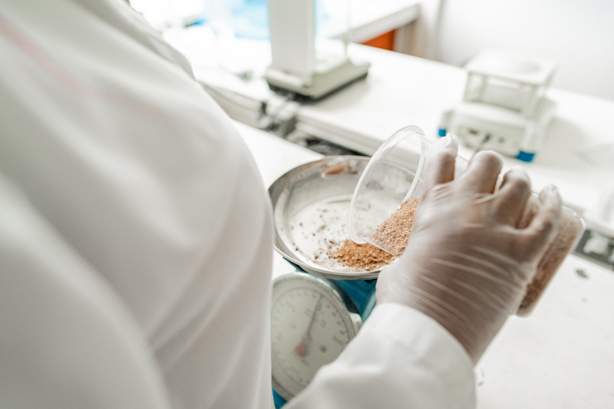 Person in a lab coat and gloves handling a small container with a white background
