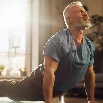 Man in a blue shirt performing a yoga pose in a bright room with large windows.